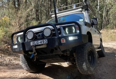 A rugged off-road vehicle equipped with spotlights and a sturdy front bumper, navigating through rough terrain in a natural setting.